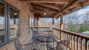 A wooden deck with a round table and chairs, a hammock, and a view of trees.