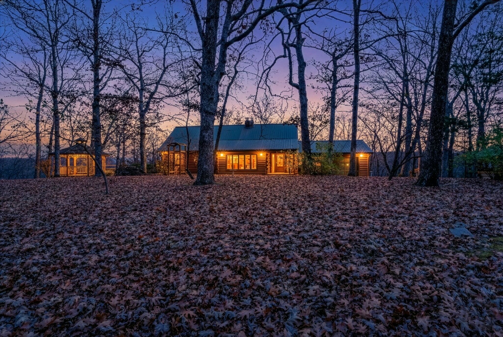 Une cabane dotée d’un grand porche à l’avant, entourée d’arbres et bordée d’un sol recouvert de feuilles.