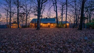 Une cabane dotée d’un grand porche à l’avant, entourée d’arbres et bordée d’un sol recouvert de feuilles.