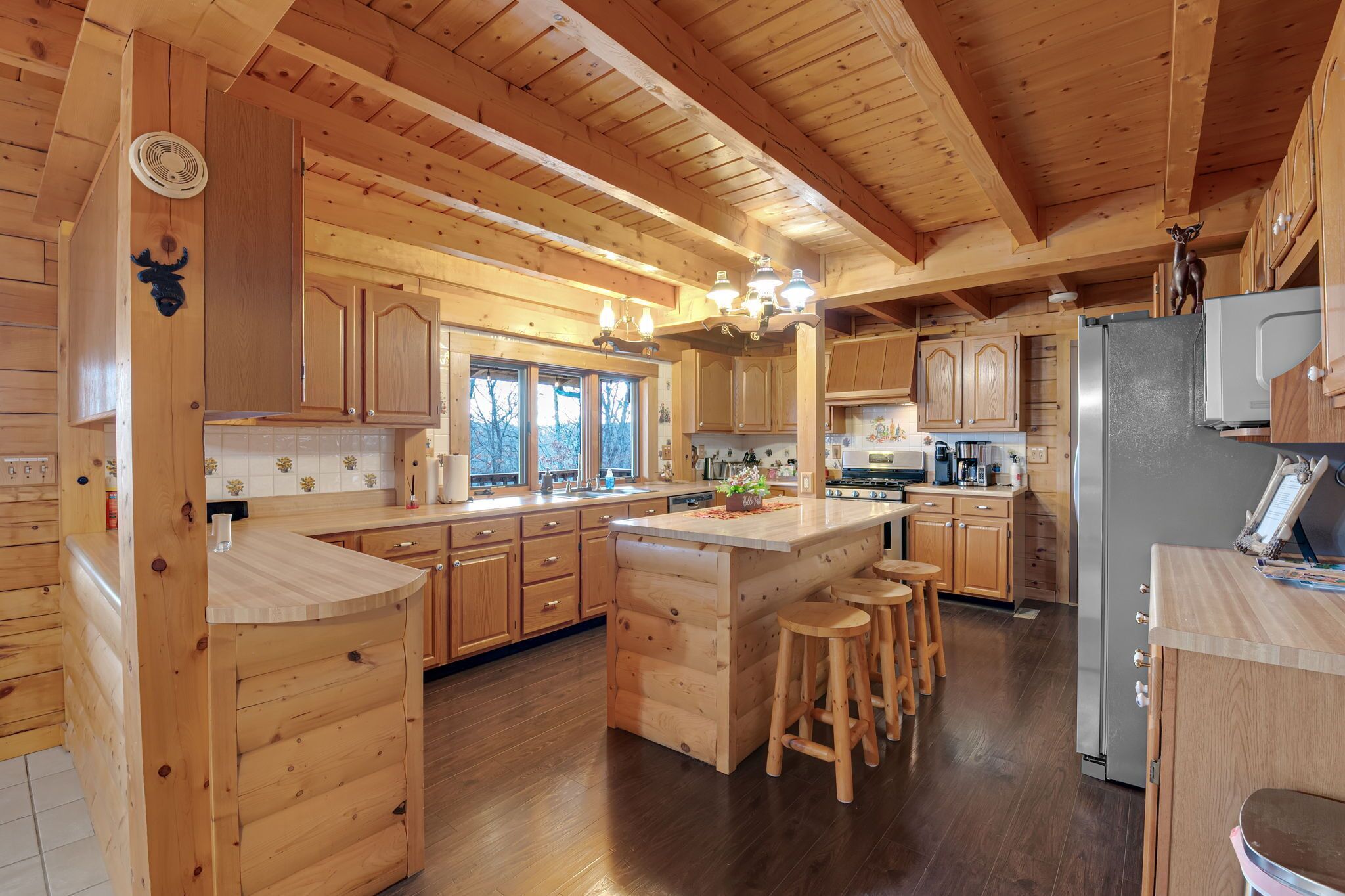 Une cuisine de style rustique, avec des éléments en bois, comprenant un îlot central, des armoires en bois et un grand réfrigérateur.