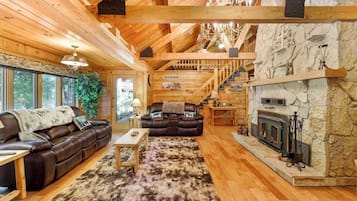 L’intérieur chaleureux d’un chalet en bois comprend une cheminée, un canapé en cuir et un escalier menant à un étage supérieur.