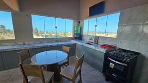 A kitchen with a round table, chairs, a gas stove, and large windows offering a view of palm trees and the ocean. - Penthouse by the Beach Near Rancho do Peixe & Jeri (Preá - CE)