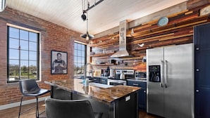 A modern kitchen with a large island, stainless steel appliances, and a rustic wooden accent wall. - Downtown Urban Loft #4 (Perryville)