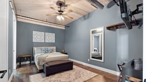 A bedroom with a bed, a bench, a ceiling fan, a mirror, and a shelf with books. - Downtown Urban Loft #4 (Perryville)