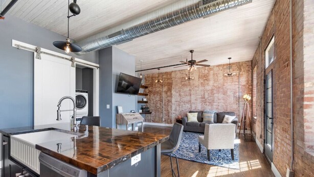A modern kitchen with a central island, a built-in washer and dryer, and a dining area with a sofa and chairs. - Downtown Urban Loft #4 (Perryville)