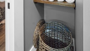 A corner with three wooden shelves against a grey wall, holding white and blue towels, and a wicker basket below. - Downtown Urban Loft above Restaurants (Perryville)