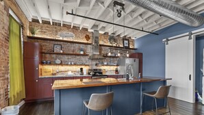 A modern kitchen with a brick wall, wooden bar counter, and bar stools. - Downtown Urban Loft above Restaurants (Perryville)
