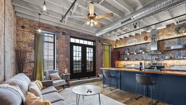 A modern kitchen with a bar area, a dining area with a sofa and chairs, and a large window with curtains. - Downtown Urban Loft above Restaurants (Perryville)