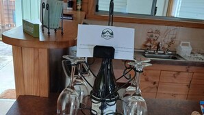 A wooden counter with a wine bottle and glasses, a welcome sign, and a menu board. - Snug Stays After Wild Days (Strahan)