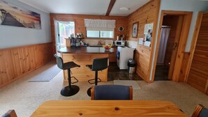 A cozy kitchen with wooden walls, a bar area, and a dining table with chairs. - Snug Stays After Wild Days (Strahan)