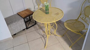 A small, yellow metal table with a glass top and two matching chairs, a small wooden stool, and a white door in a tiled room.