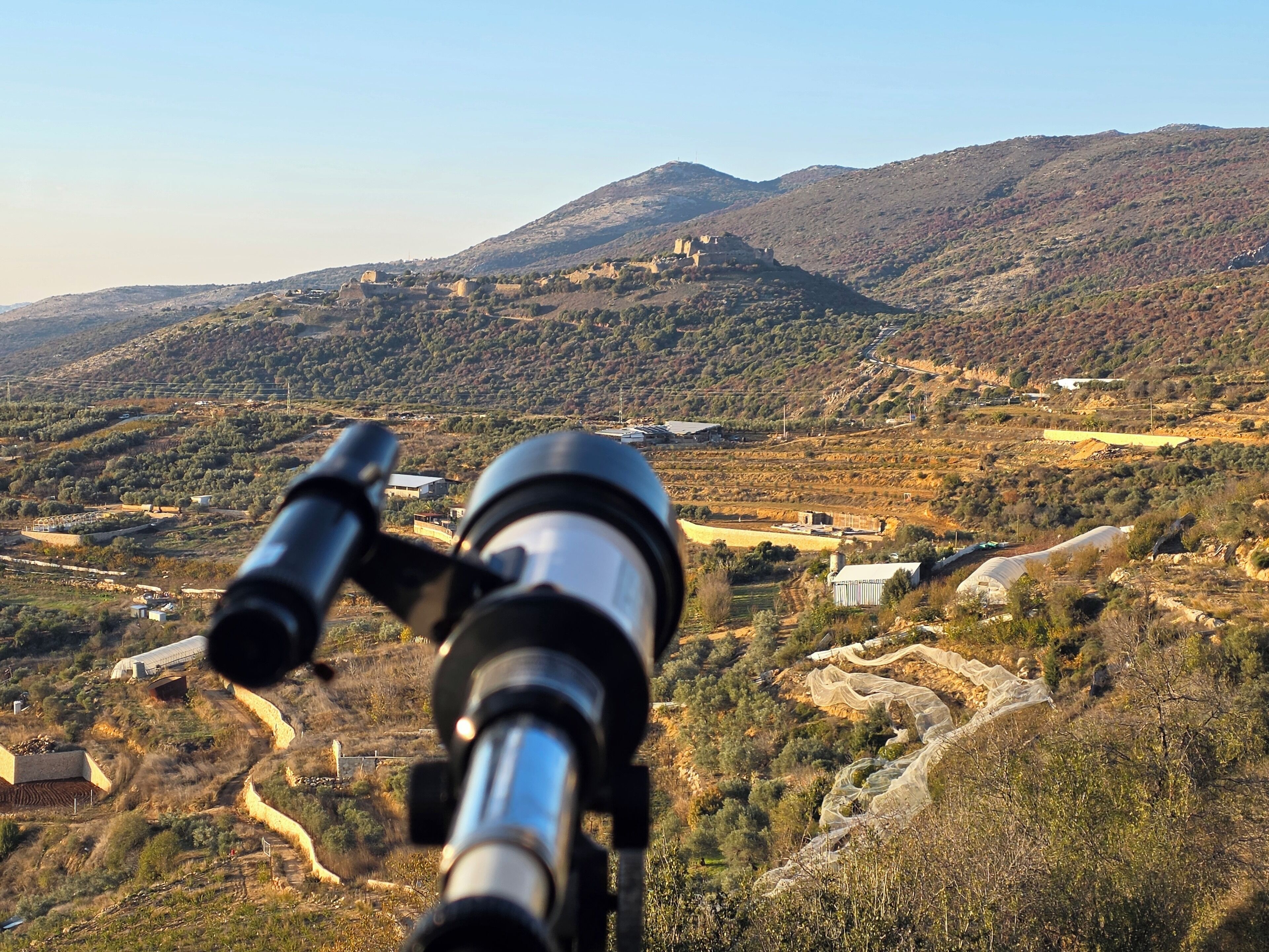 Un télescope pointé vers un paysage montagneux, avec des bâtiments et des chemins sinueux.