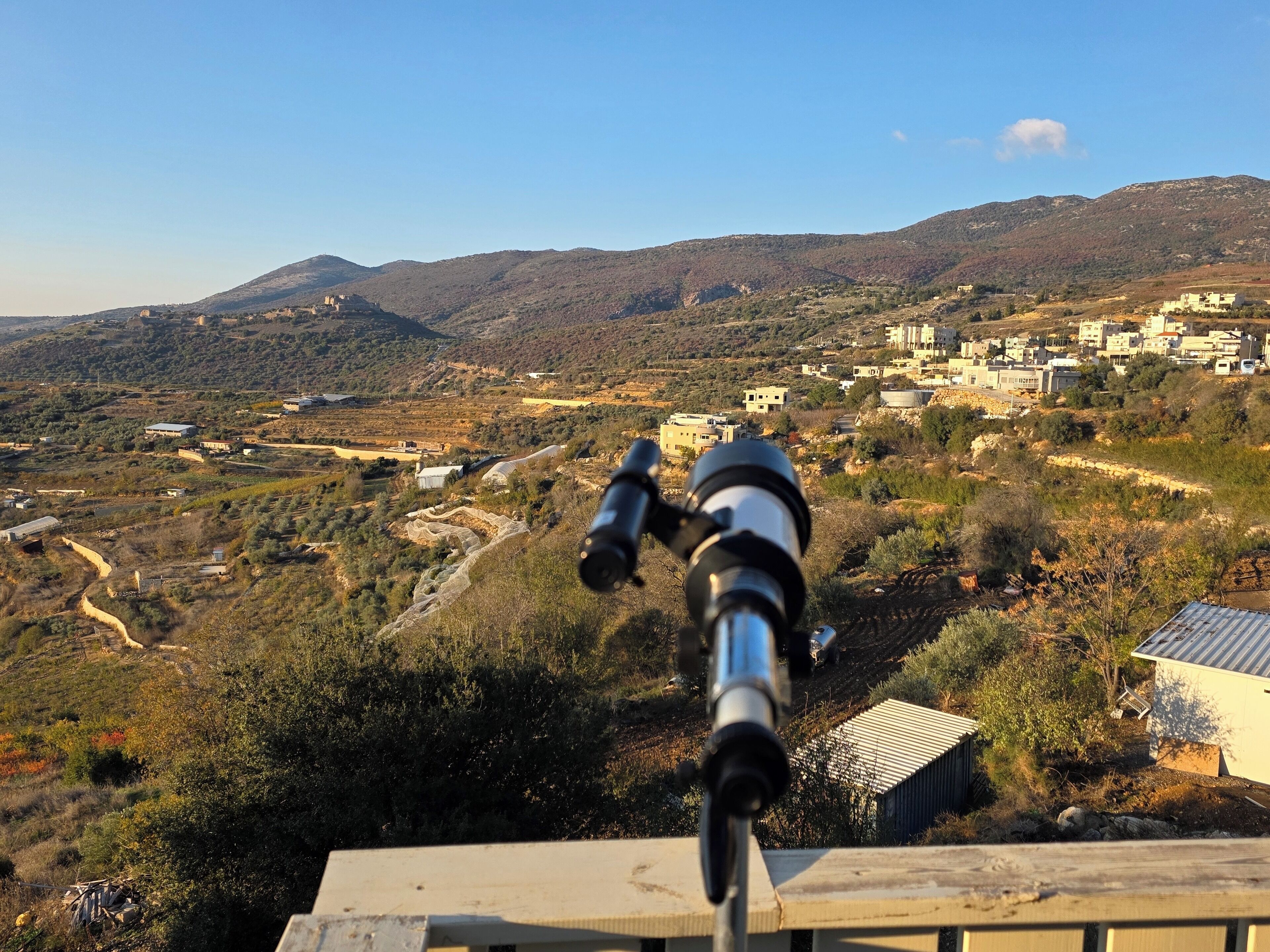 A telescope aimed at a mountainous landscape with buildings in the distance.