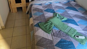 A bedroom with a bunk bed, a quilted bedspread, a green towel, and a small painting on the wall.