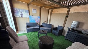 A covered outdoor seating area with a sofa, chairs, a coffee table, and a TV.