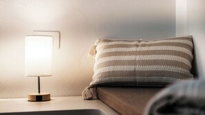 A bedside table with a lamp, a pillow, and a wall-mounted light switch. - Batèl House 5 (Como)
