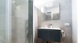 A modern bathroom with a glass shower enclosure, a vanity with a mirror, and a towel rack. - Batèl House 5 (Como)