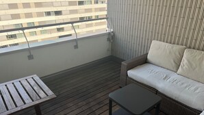 A balcony with a wooden floor, a wicker sofa with cushions, and a small table. - Modern and bright home by Prime Tower with workspaces & balcony (Zürich)