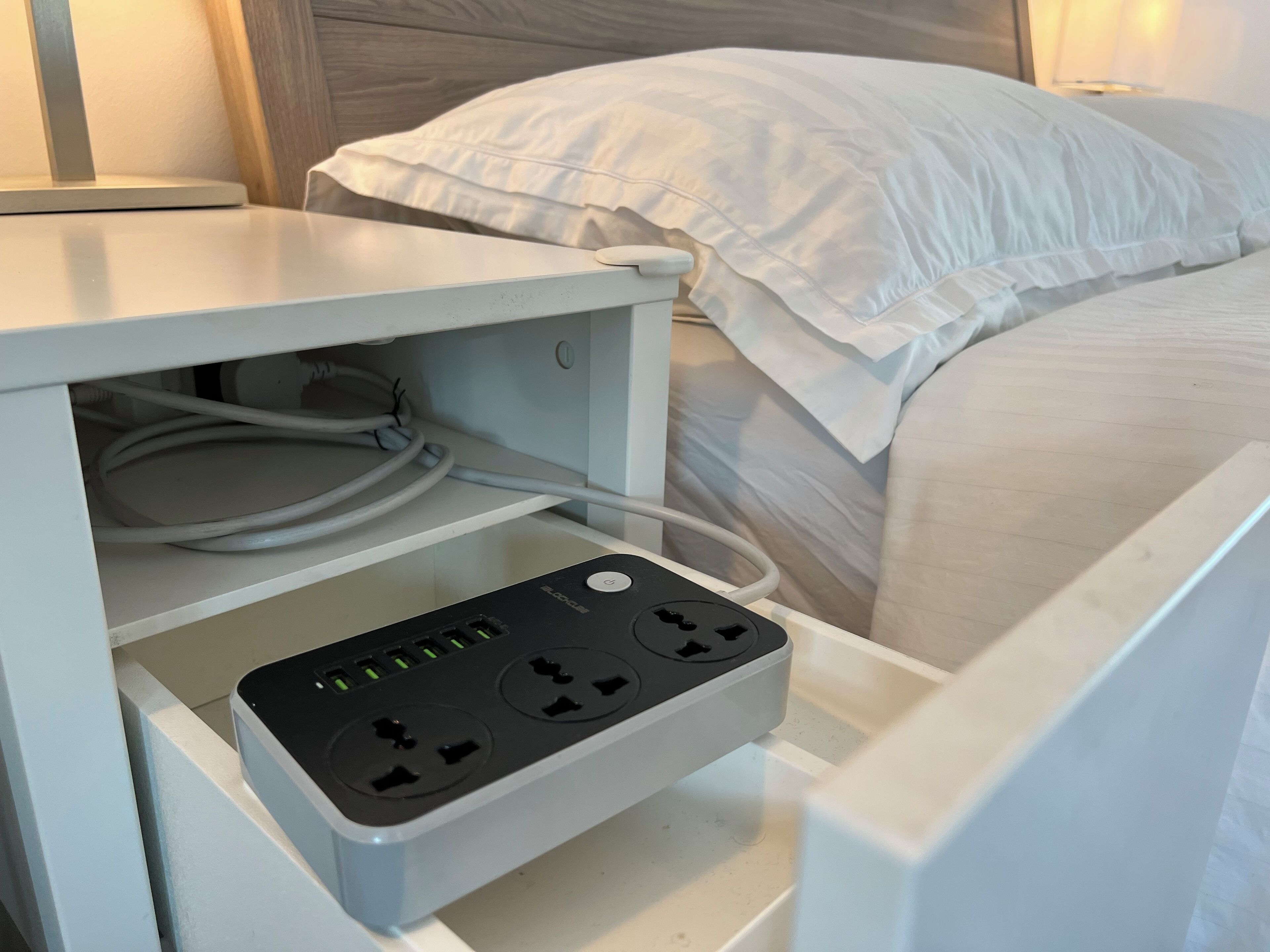 Ein Bett mit weißer Bettwäsche und ein Nachttisch mit Steckleiste.