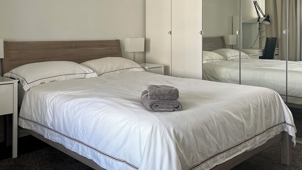 A hotel room with a large bed, a nightstand, a lamp, and a mirror. - Modern and bright home by Prime Tower with workspaces & balcony (Zürich)