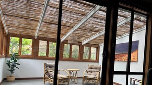 A room with a glass door leading to an outdoor area with wicker furniture and a view of greenery.