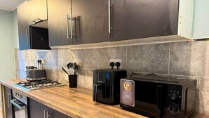 A kitchen with dark cabinets, a wooden countertop, a gas stove, a coffee maker, and a microwave. - Alat Residence (Kettering)