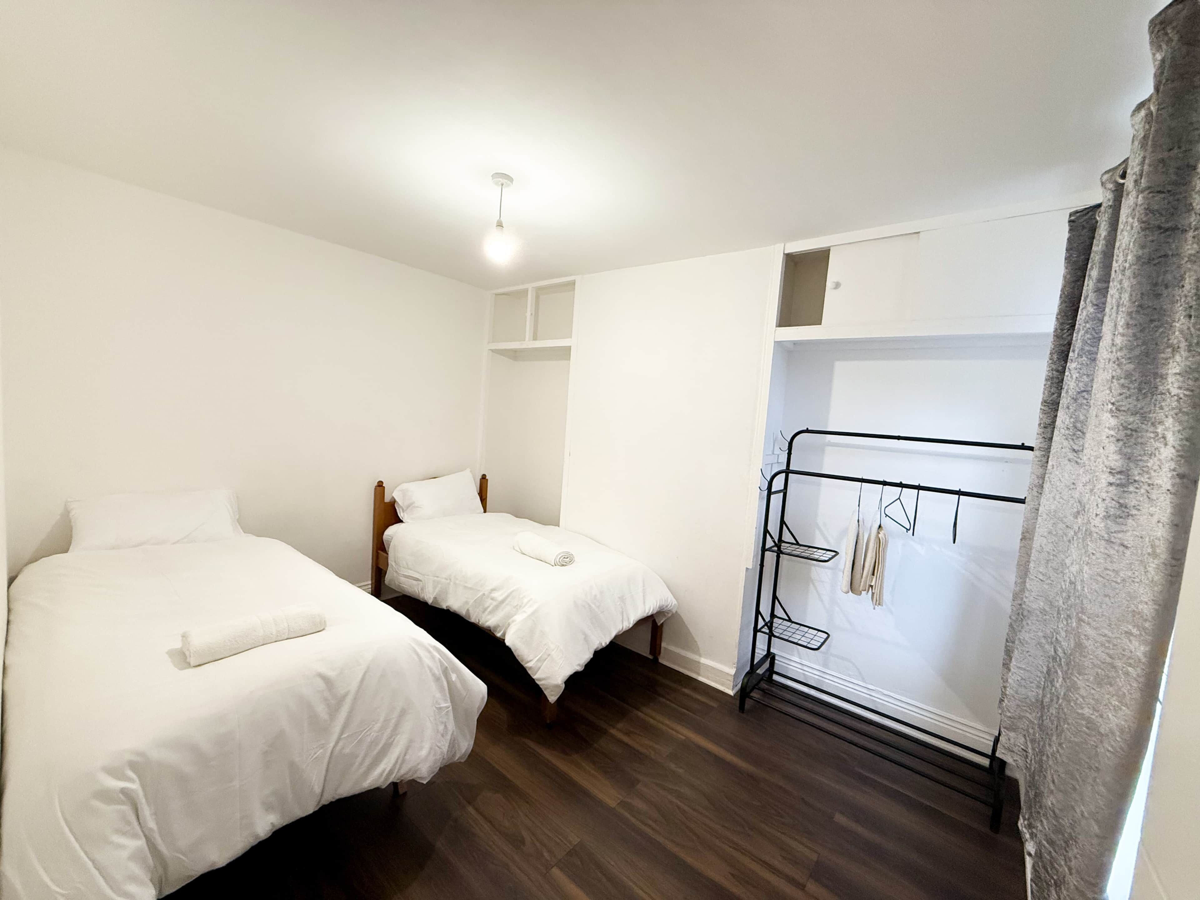 A room with two single beds, a wardrobe, and a hanging rack.