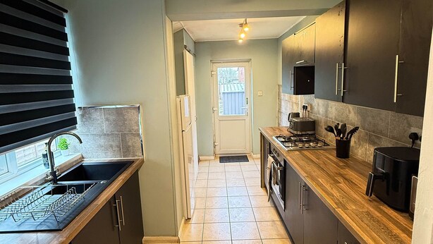 A modern kitchen with dark cabinets, a wooden countertop, a built-in oven, and a dishwasher. - Alat Residence (Kettering)