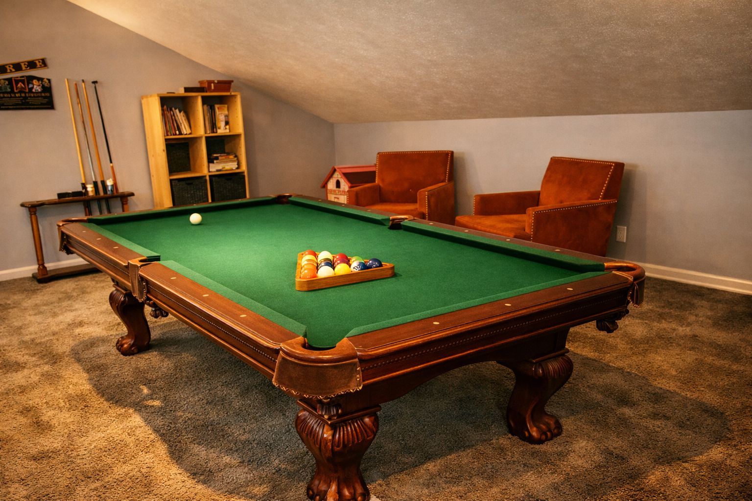 Une table de billard avec une boule blanche et un triangle de billes, entourée de deux fauteuils en cuir et d’une bibliothèque.