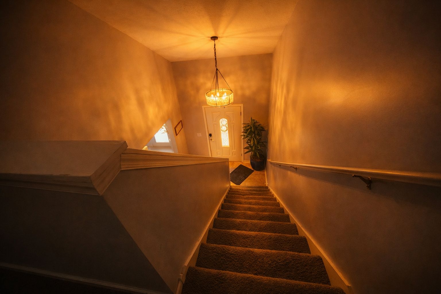 A staircase with carpeted steps, a handrail, and a hanging light fixture.