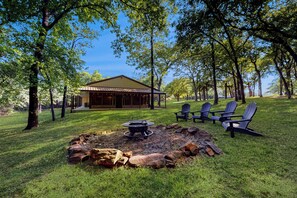 A rustic outdoor area with a fire pit, Adirondack chairs, and a building with a metal roof.