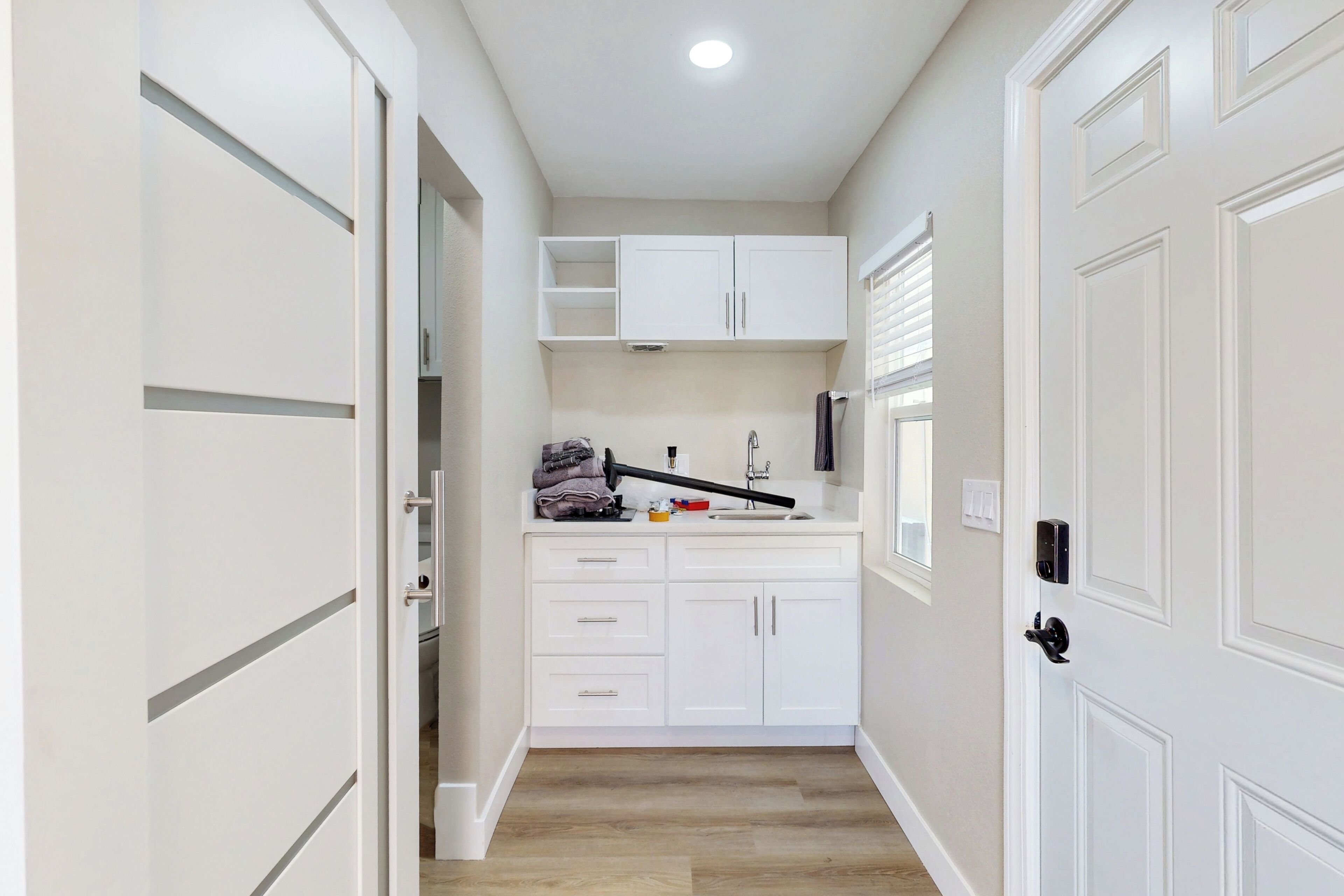 A narrow hallway leading to a kitchen with white cabinetry, a sink, and a window.
