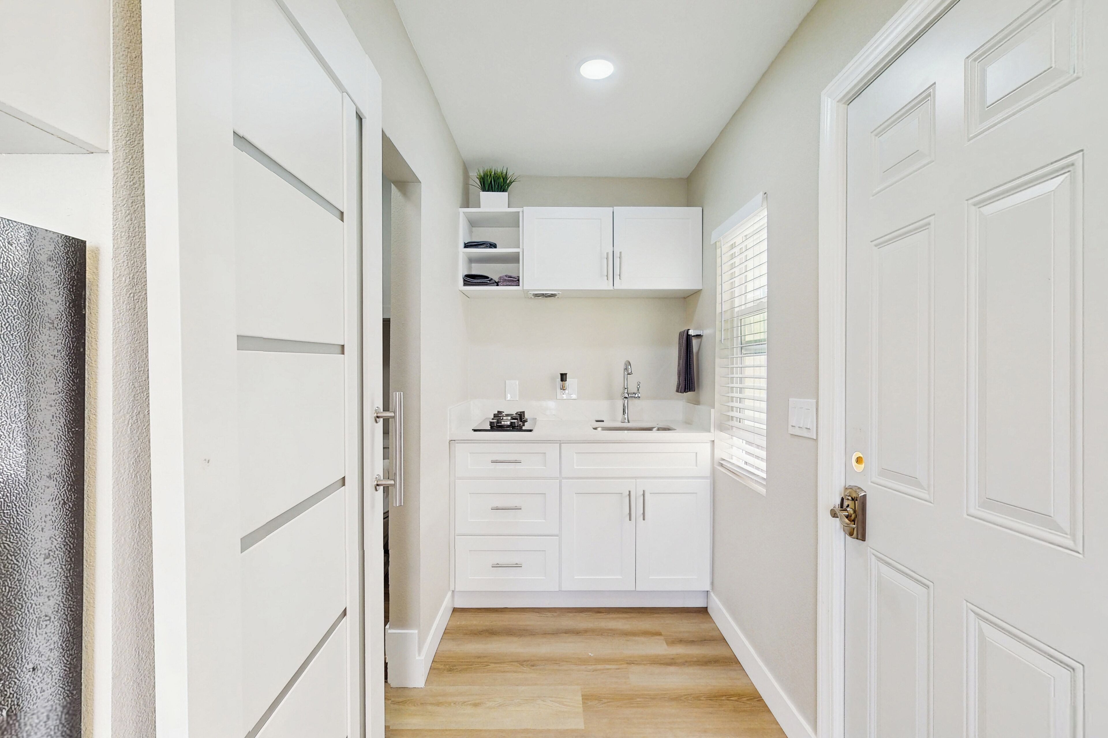 A narrow hallway with white cabinetry, a sink, and a window with blinds.