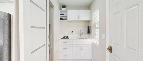 A narrow hallway with white cabinetry, a sink, and a window with blinds.