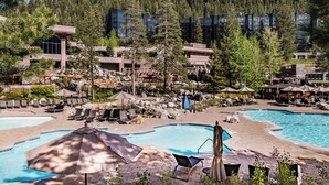 A resort with a pool area, lounge chairs, umbrellas, and a forested backdrop. - Valley-View Unit in Everline Resort: Premier Perks (Olympic Valley)