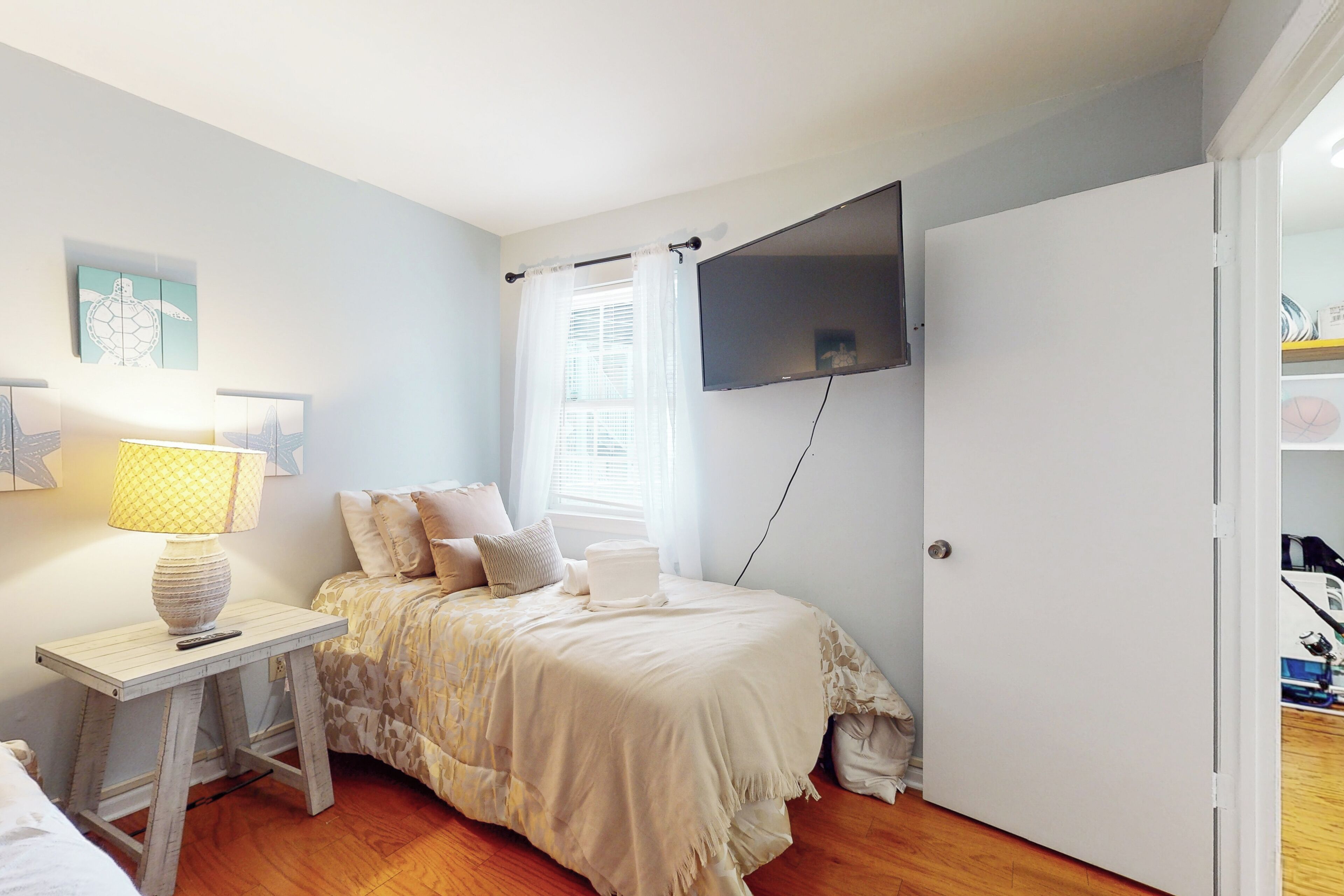 Une chambre à coucher avec un lit, une table de chevet avec une lampe, un téléviseur fixé au mur et une fenêtre avec des rideaux.