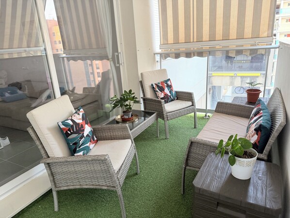A balcony with wicker furniture, a glass table, and potted plants.