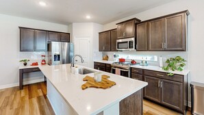 Une cuisine moderne avec des meubles de couleur bois foncé, un plan de travail blanc, des appareils en acier inoxydable et une planche à découper en bois.