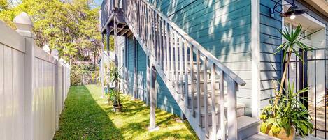 A residential property with a wooden staircase leading to a porch, a fenced yard, and potted plants.