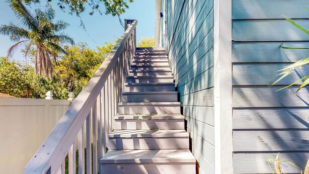 A wooden staircase with a white railing leading up to a building with blue siding.