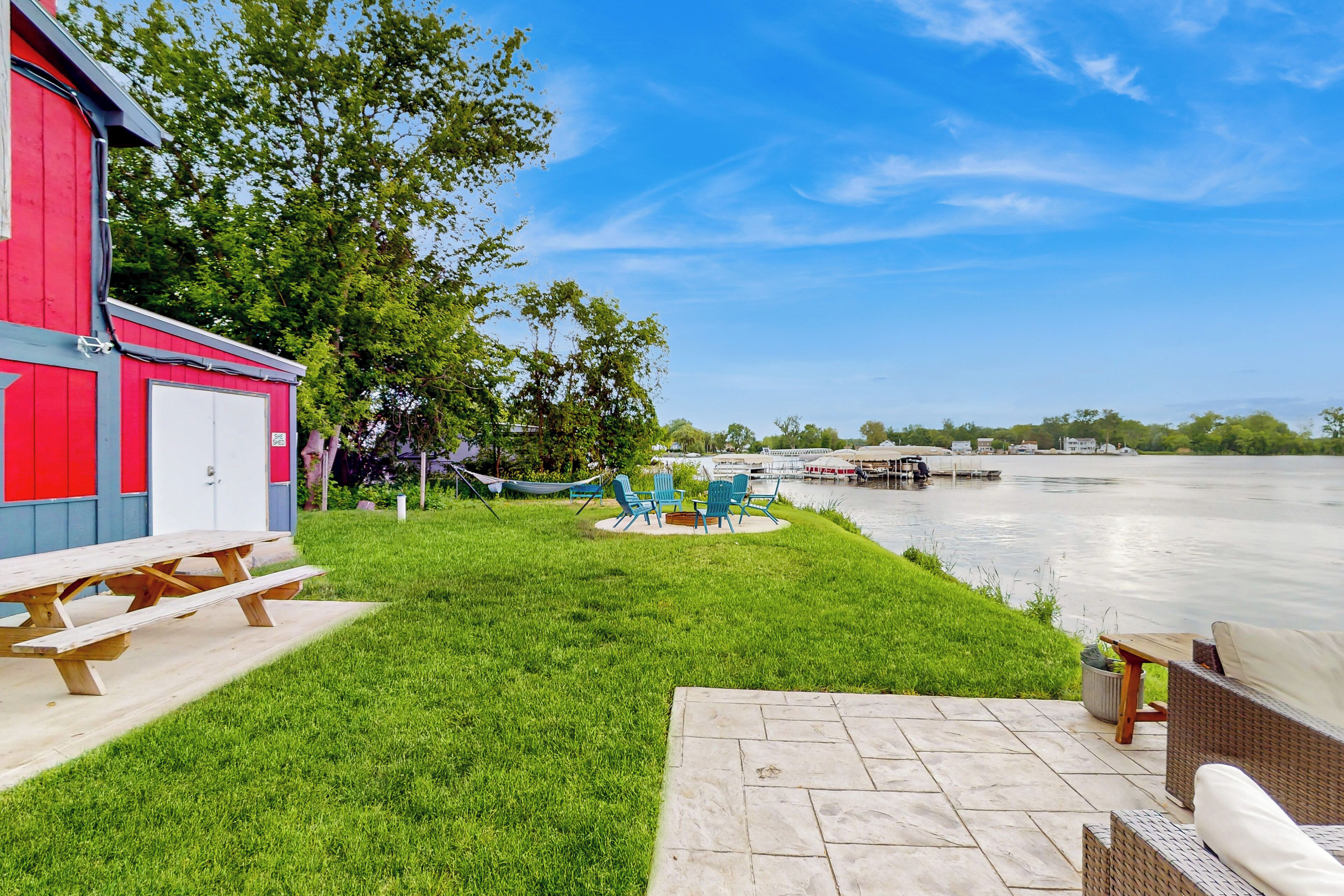 Un patio junto al río con una mesa de picnic, mobiliario exterior y un edificio rojo con una puerta blanca.