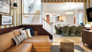 Ein Wohnzimmer mit einer Ledersofa, ein Essbereich mit grünen Stühlen und eine Treppe mit gestreiften Wänden.