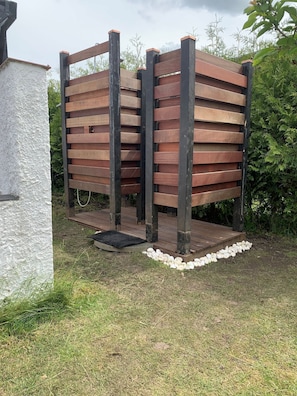 Una estructura de madera con una plataforma, rodeada por un muro blanco y follaje.