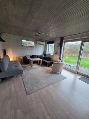 Una sala de estar moderna con un sofá seccional, una mesita y un sillón. Una ventana grande ofrece vistas al exterior.