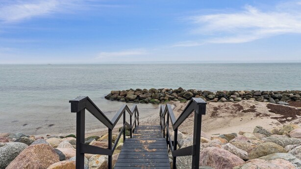 A wooden staircase leading to a beach with a rocky shoreline and calm sea.