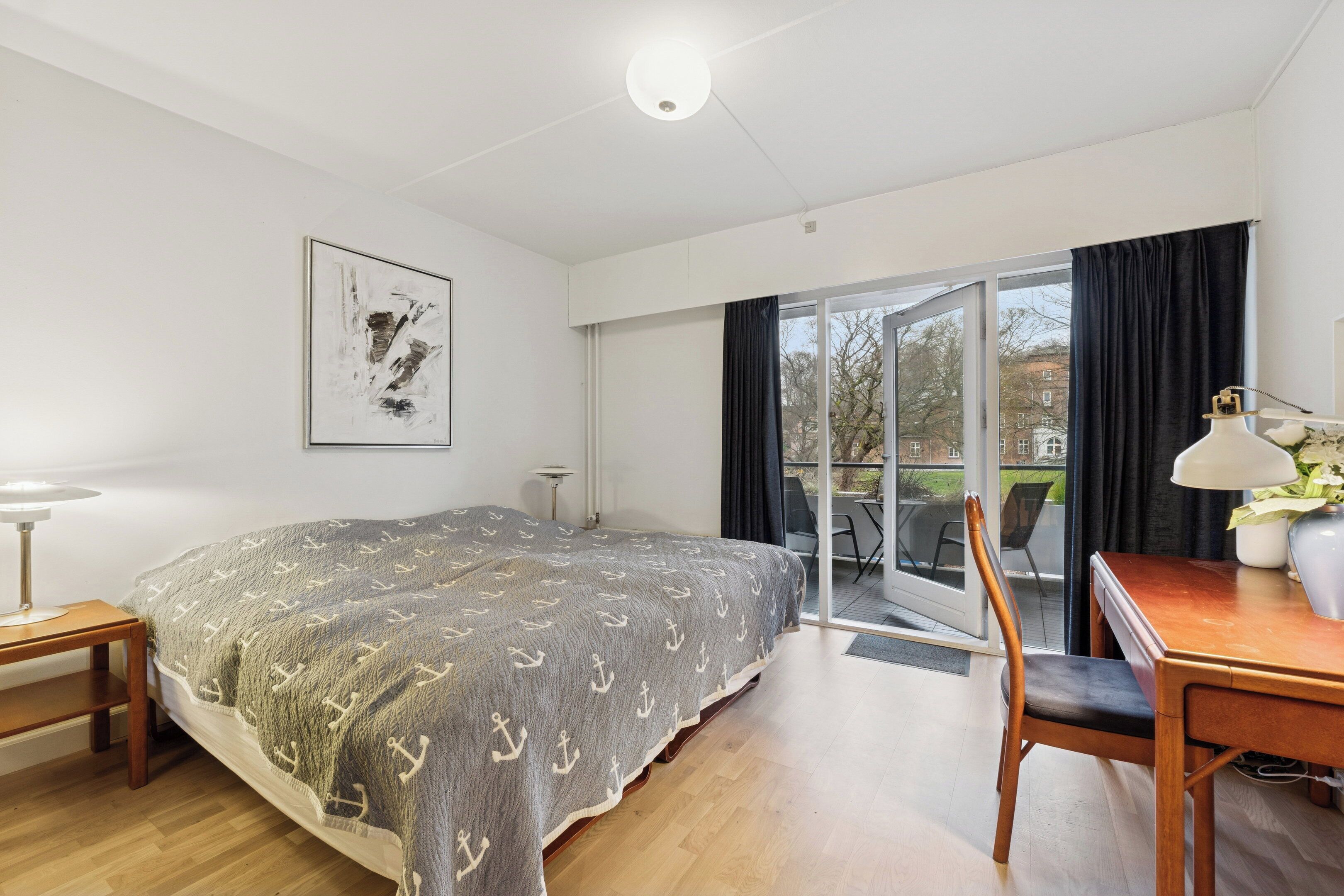 A bedroom with a bed, a desk, a chair, a lamp, and a window with curtains.