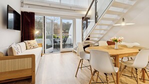 A modern interior with a wooden dining table, white chairs, a sofa, and a staircase.