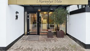 A building entrance with a sign reading 'Marienlyst Palace,' a glass door, and two potted plants.