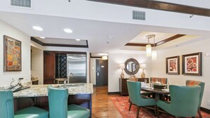 Une cuisine équipée d’un réfrigérateur en acier inoxydable, d’un plan de travail en marbre, de tabourets de bar turquoise et d’un coin repas avec une table et des chaises.