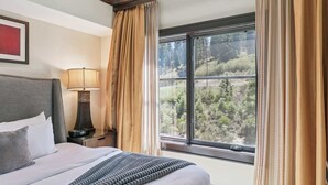 Une chambre d’hôtel avec un lit, une table de chevet avec une lampe, une fenêtre avec des rideaux et un tableau encadré au mur.